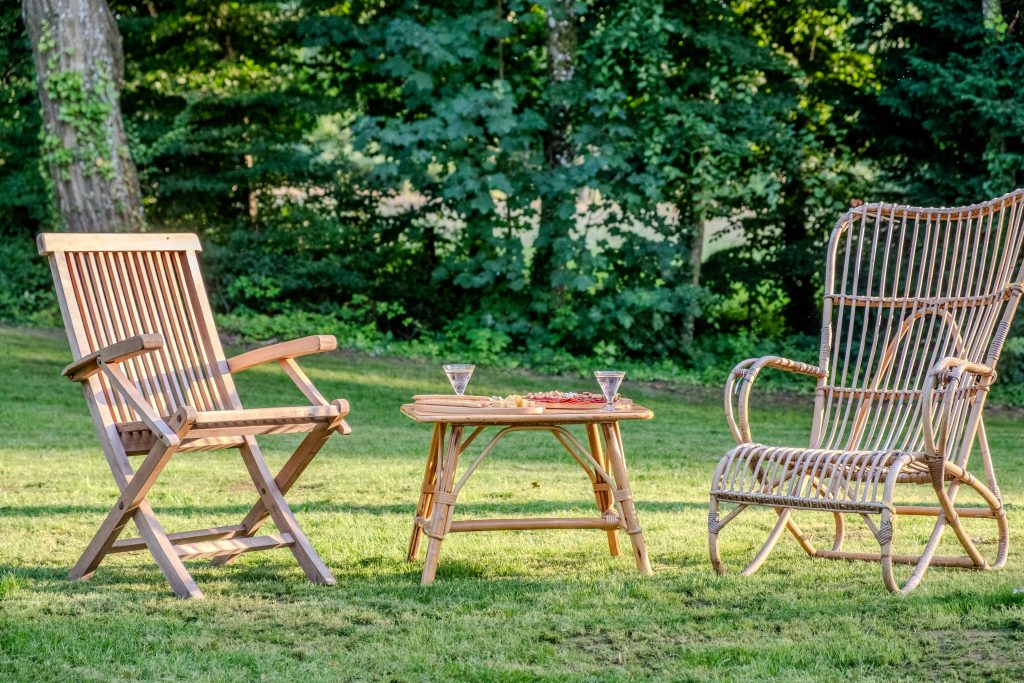 Two wooden garden chairs and a small table with drinks set on the lawn at Château Guillermo, surrounded by lush greenery in the French Ardennes.